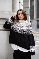 Sweater de lana con diseño de jacquard en la parte superior, cuello redondo, mangas largas y puños acanalados. Presenta un corte holgado con tajos laterales y un diseño ligeramente más corto en la parte delantera.