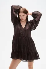 Vestido corto de manga larga con cuello en V y cierre frontal de botones. Presenta un diseño holgado con falda de volado en el ruedo y un estampado sutil de rayas verticales brillantes sobre fondo oscuro.