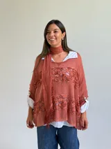 Sweater de punto color naranja con diseño holgado, que incorpora franjas horizontales de encaje con motivos florales. Presenta mangas tres cuartos con puños abotonados y se complementa con una bufanda del mismo tejido y color.