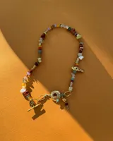 Collar corto de estilo artesanal, compuesto por una variedad de piedras naturales en tonos tierra, verdes, rojos y amarillos, intercaladas con pequeñas perlas de río. Presenta dijes de bronce macizo con formas orgánicas, incluyendo una figura de pez y un dije circular central, unidos por un cierre de barra y argolla.