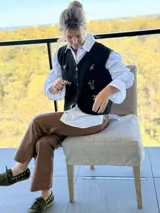 Chaleco negro con cierre frontal de botones, decorado con flores bordadas a mano y costuras decorativas en los bordes.