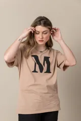 Remera gris con estampa de la letra M en negro y cadena plateada en el cuello.