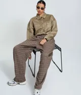 Pantalón de vestir de corte barrel, tiro alto con pliegues delanteros y pierna ancha, confeccionado en tejido con estampado de cuadros en tonos marrones y rojizos.