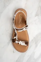 Sandalias con estampado animal print de vaca, con suela marrón y hebilla ajustable.