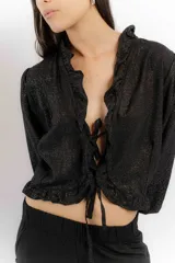 Blusa negra de lino con acabado brillante, de manga larga abullonada, escote con volados y cierre frontal con tiras para anudar.