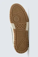 Zapatilla deportiva de estilo retro con diseño de paneles en tonos crema y blanco, detalles en verde oscuro y suela de goma color caramelo.