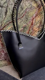 Cartera de cuero mediana con manijas largas, diseño con borde superior en corte en V y terminación artesanal con costuras contrastantes.