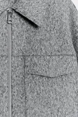 Cazadora de textura suave con cuello solapa, manga larga y cierre frontal con cremallera metálica. Presenta dos bolsillos de plastrón con solapa en la parte delantera.