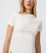 Remera de algodón con elastano color blanco, de corte ajustado, manga corta y cuello redondo. Presenta un detalle frontal de botones dispuestos en forma de estrella.