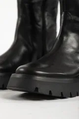 Botas bucaneras de cuero negro con caña alta, suela track robusta y cierre lateral.