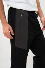 Pantalón de jogging negro con paneles grises en la parte superior, cintura elástica con cordón ajustable y puños elásticos en los tobillos.