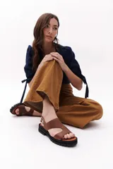 Sandalia de cuero color camel con diseño de tiras anchas cruzadas en el empeine, cierre con hebilla metálica lateral y suela de goma tipo tractor en color negro.