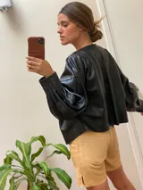 Campera de cuero con silueta oversize y corte levemente corto. Presenta cierre frontal metálico, cuello a la base y mangas amplias con detalles trenzados y recortes que aportan textura.