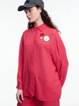 Camisa color coral de calce relajado con abertura en la espalda y mangas largas. Confeccionada en tejido liviano de lino y viscosa. Incluye tres pins decorativos.