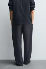 Pantalón negro de corte relajado con cintura elástica ajustable y pliegues en la parte delantera. Presenta bolsillos laterales y bolsillos traseros de parche.