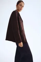 Campera tipo blazer o chaqueta de tejido suave con acabado cepillado, color marrón oscuro. Presenta solapas de muesca, cierre frontal de tres botones y dos bolsillos parche grandes en la parte delantera inferior.