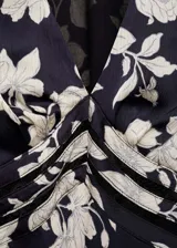 Vestido midi de corte evasé con estampado floral en blanco y negro. Presenta cuello de pico, mangas cortas y detalles de blonda en la cintura.