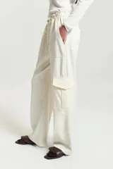 Pantalón babucha color crudo de gabardina con elástico en la cintura, cordón ajustable tipo zapatilla, bolsillos plaque y bolsillos cargo grandes en el delantero.