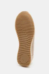 Zapatilla deportiva tipo running en tonos beige y crema, con combinación de materiales como gamuza y tela. Presenta pespuntes decorativos en el cuerpo, cierre de cordones y punta redonda. La suela tiene una altura de 3 cm.