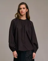 Blusa fluida color marrón oscuro, con cuello mao y mangas largas abullonadas terminadas en puño ajustado.