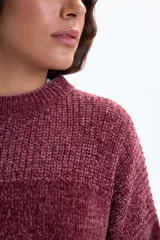 Buzo de punto chenille en color bordó, con cuello redondo, mangas largas y aberturas laterales en el ruedo. Presenta un diseño de textura acanalada en el cuello, hombros y puños.