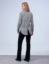 Camisa estampada blanca y negra con cuello clásico, abertura frontal con botones ocultos y mangas largas con puños abotonados.