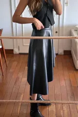 Falda asimétrica negra de cuero sintético, con diseño irregular, más corta en el lateral y con una caída más larga del otro.