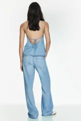 Pantalón de jean estilo pijamero de tiro medio, con cintura elástica ajustable mediante cordones. Presenta corte recto, bolsillos laterales y cierre frontal con cremallera y gancho metálico.