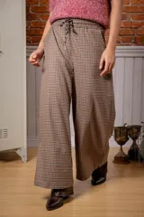 Pantalón de corte ancho y tiro alto, con estampado de cuadros pequeños en tonos marrones y negros. Cuenta con cintura elástica y cordón ajustable.