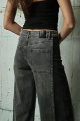 Jean de corte wide leg en color gris lavado, con diseño bicolor que presenta un panel lateral en un tono de gris más oscuro. Posee tiro medio, cierre frontal con botón y bolsillos laterales.