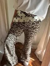 Cinturón ancho de cuero color crema con remaches metálicos plateados.