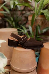 Zuecos de gamuza color marrón con taco cuadrado bajo y tira sobre el empeine decorada con tachas metálicas.