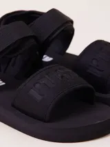 Sandalias de plataforma plana en color negro, confeccionadas en EVA con tiras anchas ajustables mediante velcro y detalle de logo en relieve.