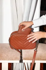 Cartera bandolera negra con diseño capitoneado en forma de V, correa de cuero y cadena plateada, cierre metálico y doble bolsillo interior.