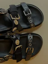 Sandalias de cuero marrón, con diseño de triple tira con hebillas, detalles de tachas y apliques de pelo con estampado animal print.