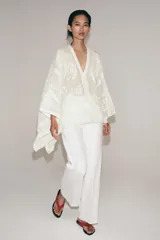 Blusa tipo capa de algodón con escote en pico y mangas largas amplias. Presenta bordados florales a tono en toda la prenda, bajo asimétrico y cierre frontal con botones.