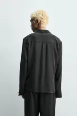 Camisa de corte relajado confeccionada en tejido fluido con mezcla de viscosa y lyocell. Presenta cuello polo, manga larga con puños abotonados y un diseño cruzado con cierre frontal de botones.