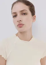 Camiseta cruda de manga larga con diseño ajustado, cuello redondo y terminaciones con ondas delicadas en contraste marrón en el cuello y el ruedo.
