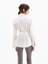 Camisa Oslo de poplín de algodón color blanco, con silueta estructurada, cuello camisero amplio, manga larga y cinturón ancho incorporado con hebilla rectangular forrada.