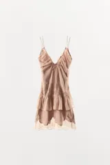 Vestido corto de satén con escote en pico y tirantes finos. Presenta un diseño con superposición de capas, detalle de lazada frontal y aplicaciones de encaje a tono en el cuerpo y el bajo con terminación en ondas.