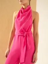 Mono fucsia con escote halter, espalda descubierta, lazo en la cintura y pantalón palazzo con tajos laterales.