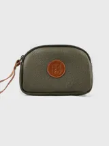 Neceser de cuero color verde oliva, con textura granulada y cierre superior. Presenta un parche circular de cuero marrón con un escudo grabado en el centro. Incluye una correa de muñeca de cuero marrón.