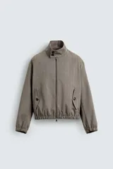 Cazadora cropped de hombre con tejido de estructura espiga. Presenta cuello subido con cierre de botones, cierre frontal de cremallera, bolsillos laterales con solapa y acabados elásticos en puños y cintura.