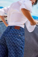 Jean de tiro bajo y corte oversize, confeccionado en denim azul con monograma grabado a láser en toda la prenda. Presenta doble botón metálico en la cintura y diseño de cinco bolsillos.