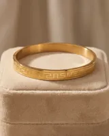 Esclava rígida de acero con baño de oro y diseño grabado de guarda griega.