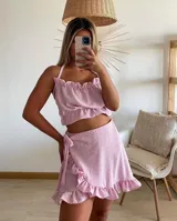 Conjunto de dos piezas en tela plumeti color rosa, compuesto por un top corto con cuello halter y volados, y una pollera corta tipo pareo con volados en el ruedo y lazo lateral.
