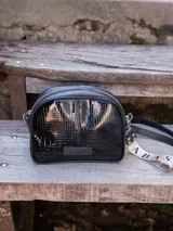 Bandolera pequeña de cuero negro con textura tipo cocodrilo, correa larga ajustable y llavero con el logo de la marca.