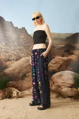 Pantalón de corte holgado y tiro medio, con cintura elástica y cordón de ajuste. Presenta un estampado geométrico multicolor sobre fondo negro.