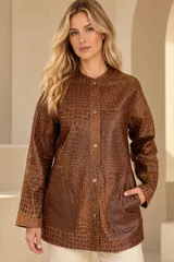 Camisa de cuero color marrón, de corte recto y largo medio, con cuello redondo a la base, cierre frontal con broches metálicos y bolsillos aplicados en los laterales.