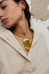 Gargantilla rígida de metal dorado con dije central de diseño orgánico y textura irregular. El diseño permite múltiples usos, incluyendo la opción de utilizar la gargantilla sola o con el dije.